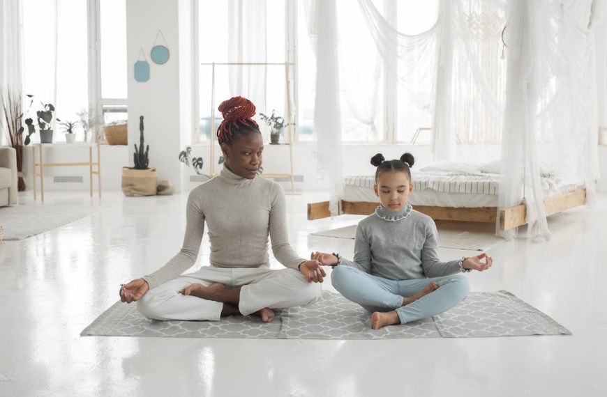 Young black mother practicing yoga with daughter in light bedroom